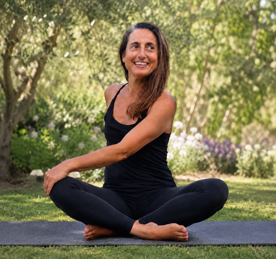 Sophie de Viveiros, professeure de yoga, assise en tailleur et souriante dans un jardin